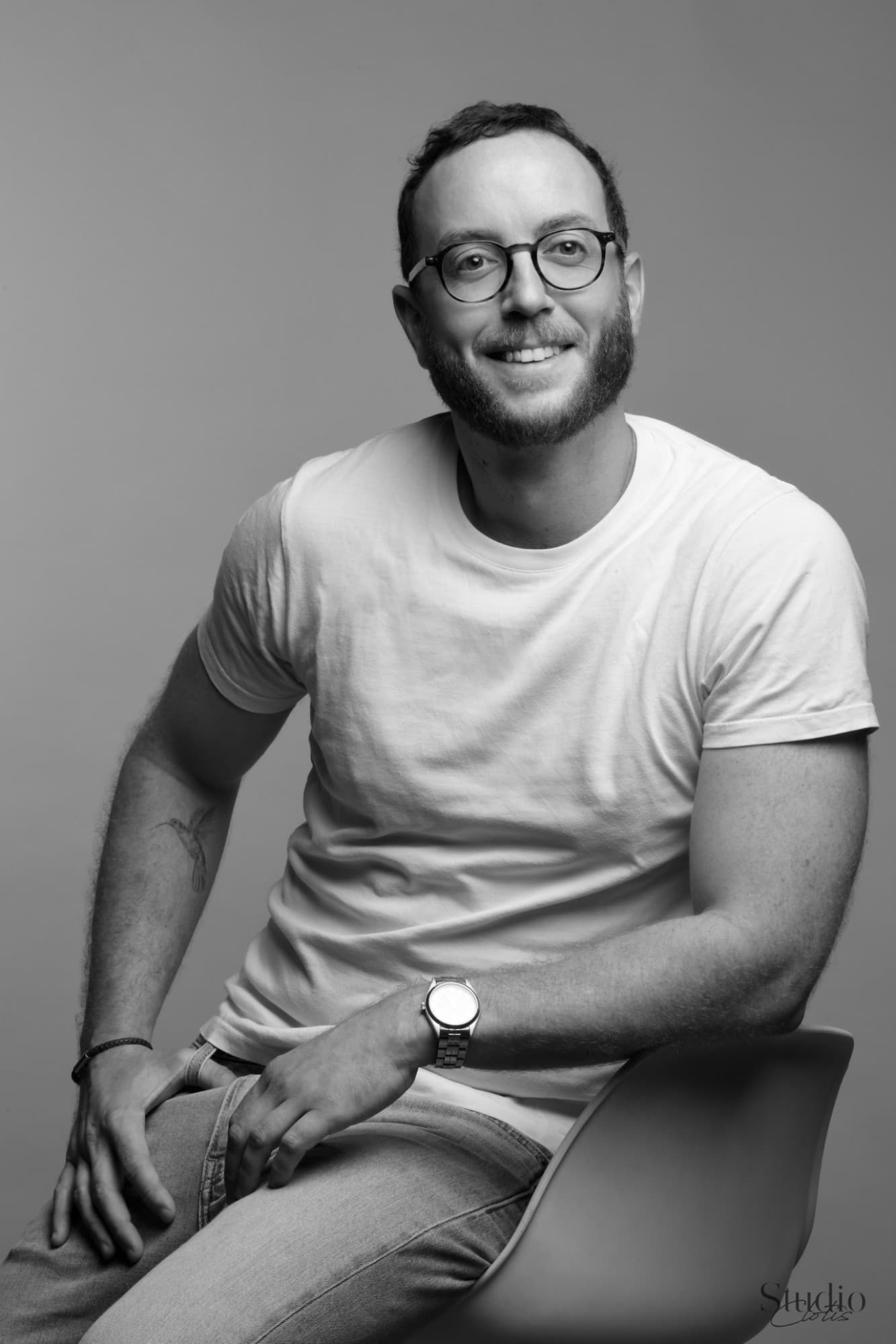Portrait en noir et blanc de Thibault Gèze, souriant, assis sur une chaise.